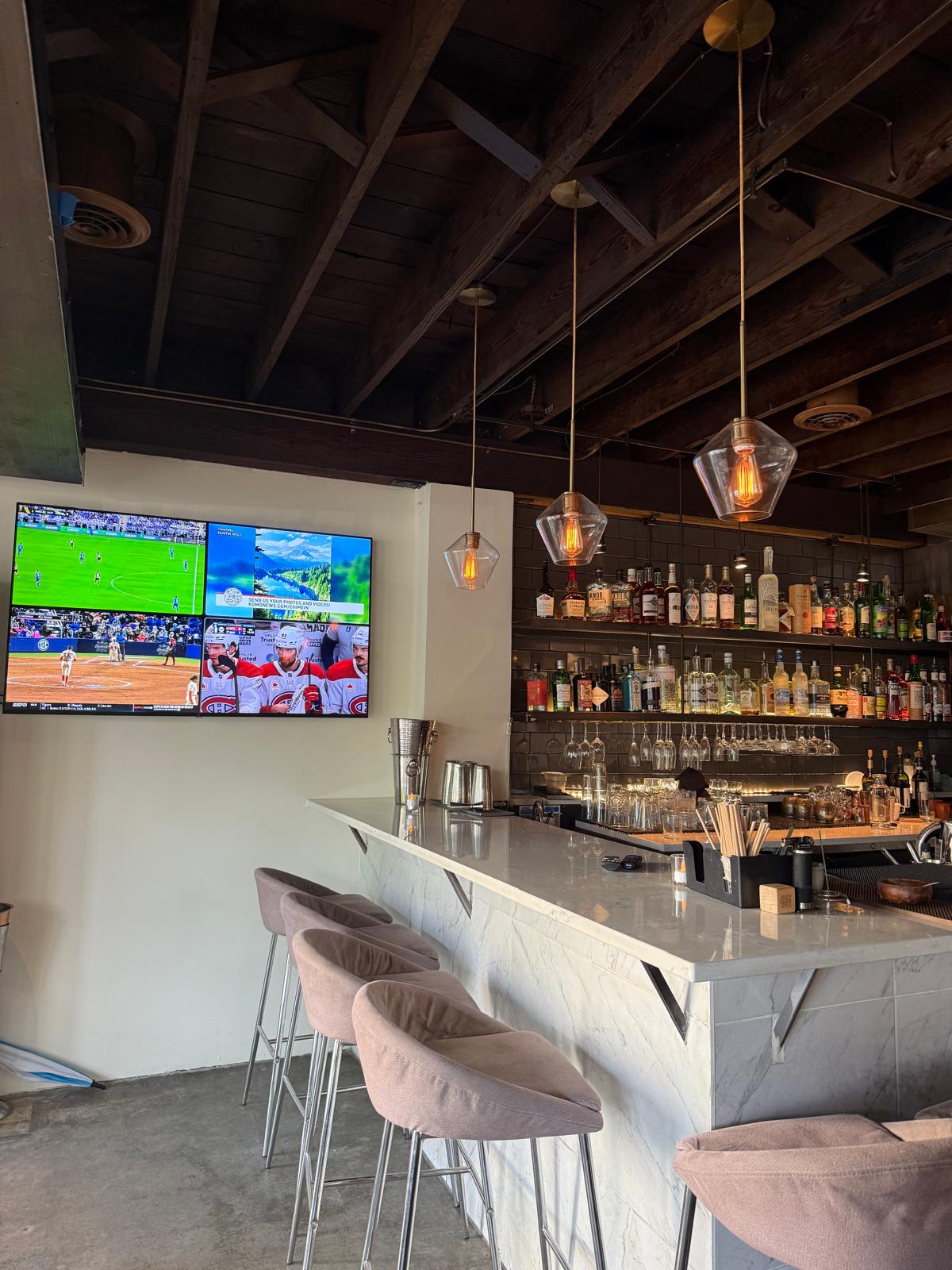 The bar — TVs, marble counter, blush bar stools